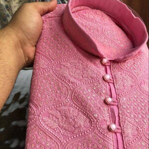 Puede incluir: Una kurta bordada de color rosa con cuello alto y cierre de botones. La tela tiene un delicado patr&oacute;n floral y est&aacute; adornada con peque&ntilde;as lentejuelas.