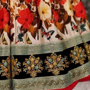 Pu&ograve; includere: Una gonna con stampa floreale bianca e rossa con un bordo nero e argento. La gonna ha uno strato di paillettes e ricami intorno al fondo.