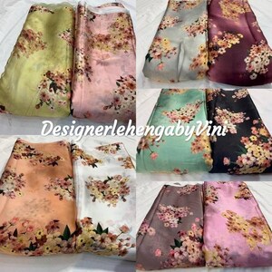 May include: Assortment of ten floral printed fabrics in various colors, including green, pink, white, orange, gray, and black. The fabric has a satin finish and features a floral print with a blurred effect. The fabric is arranged in pairs, with each pair featuring a different color and pattern. The text "Designerlehenga by Vini" is visible in the center of the image.