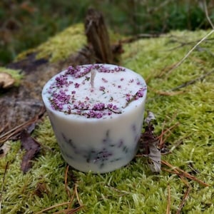 May include: A white candle with a purple and green floral design. The candle is sitting on a bed of green moss.