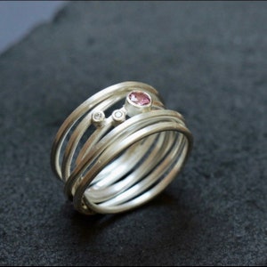 May include: A silver ring with multiple bands, featuring a pink gemstone and two smaller white gemstones.