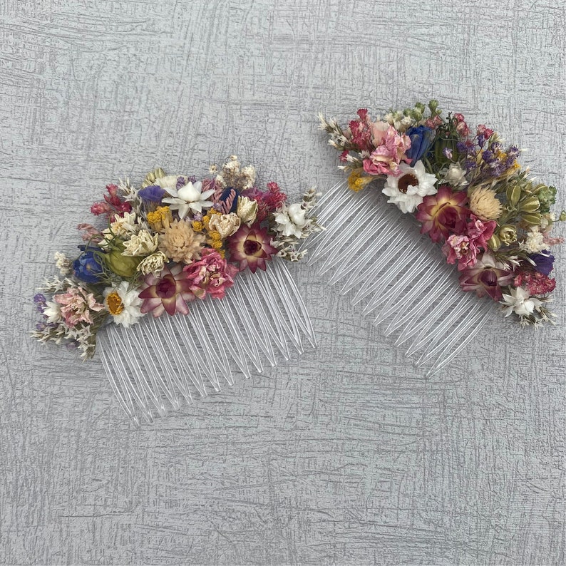 May include: Two hair combs with dried flowers. The combs are clear plastic and the flowers are a mix of pink, purple, white, and yellow.