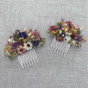May include: Two white hair combs decorated with dried flowers. The flowers are a mix of white, pink, purple, and yellow.
