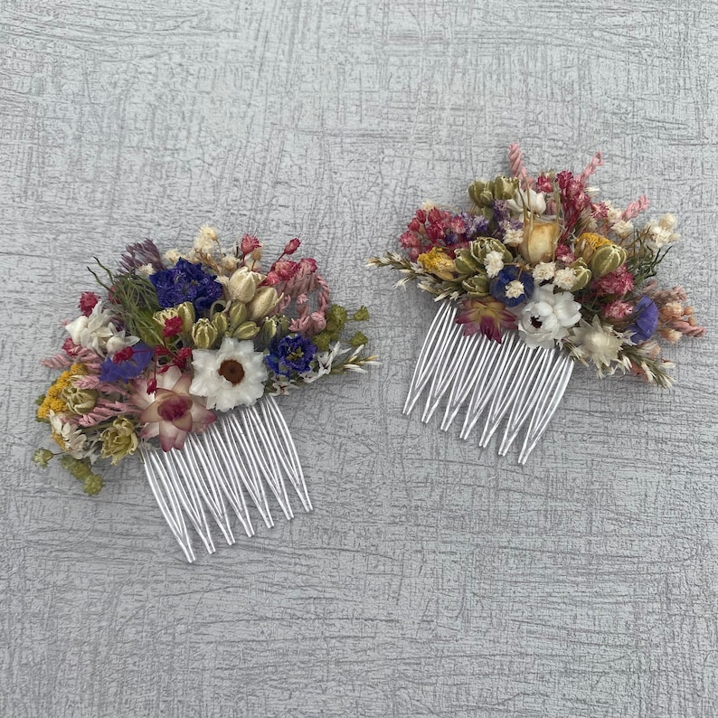 May include: Two white hair combs decorated with dried flowers. The flowers are a mix of white, pink, purple, and yellow.