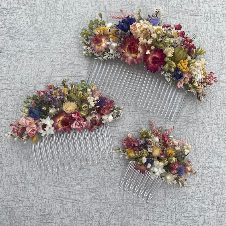 May include: Three hair combs decorated with dried flowers. The combs are made of clear plastic and have a comb-like design. The flowers are a mix of pink, red, yellow, white, and blue.
