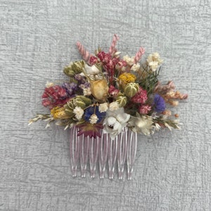 May include: A pink hair comb decorated with dried flowers in shades of pink, white, yellow, green, and purple.