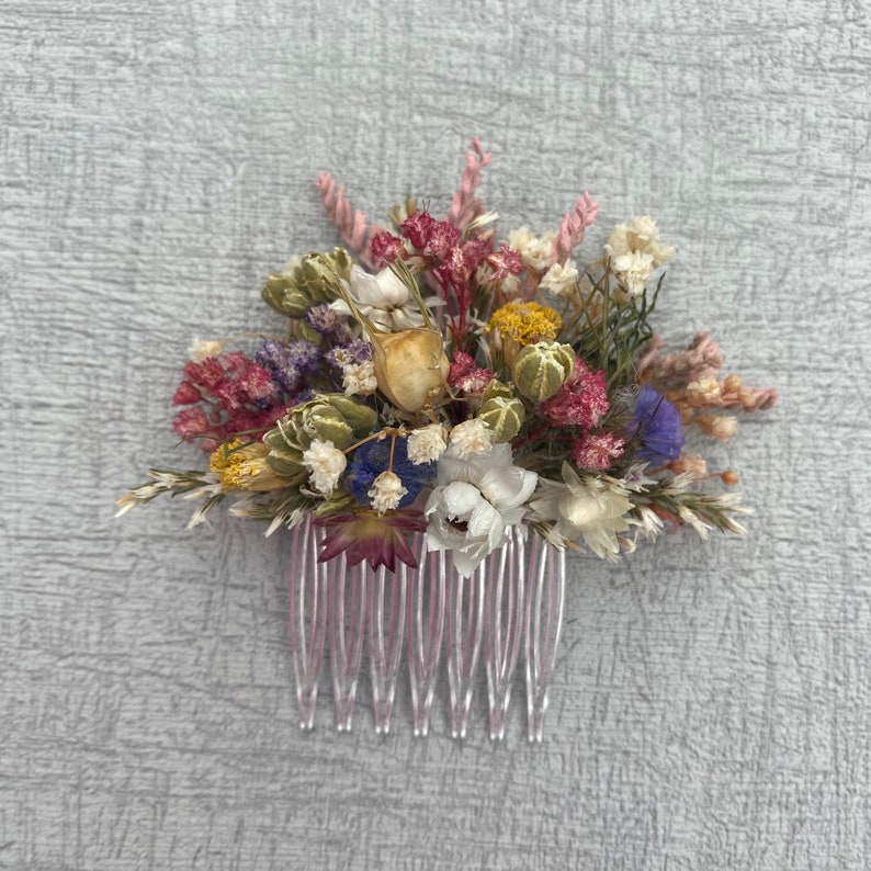 May include: A pink hair comb decorated with dried flowers in shades of pink, white, yellow, green, and purple.