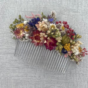 May include: A silver hair comb decorated with dried flowers in shades of pink, red, yellow, white, and blue.