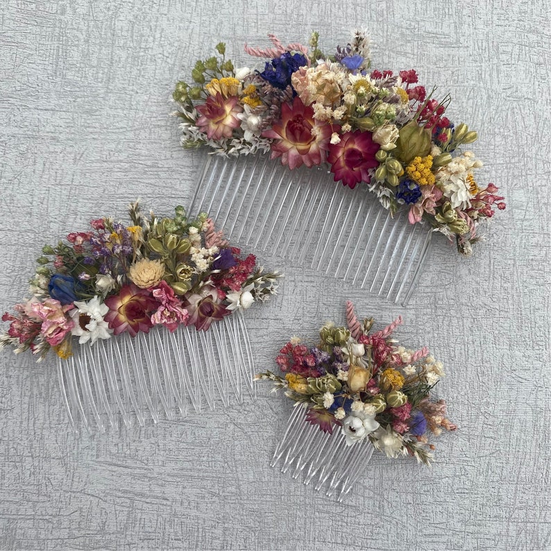 May include: Two hair combs decorated with dried flowers. The larger comb has a mix of pink, red, yellow, and white flowers. The smaller comb has a mix of pink, white, and yellow flowers.