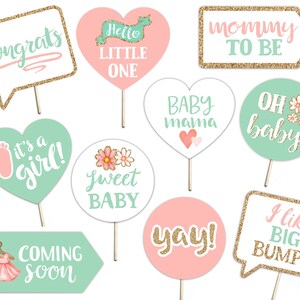 Op de afbeelding: Een set van 10 fotobooth-rekwisieten voor een babyshower in roze en groen. De rekwisieten bevatten zinnen zoals "Gefeliciteerd", "Hallo kleine", "Mama in wording", "Het is een meisje", "Zoete baby", "Baby mama", "Oh baby", "Hoera", "Binnenkort", en "Ik hou van grote buiken".