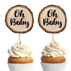 May include: Two printable cupcake toppers with a woodgrain background and the text "Oh Baby" in black. The toppers are on top of cupcakes with white frosting.