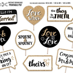 May include: A collection of wedding photo booth props with gold glitter accents. The props include signs with phrases like "Love Wins," "Here Come the Brooms," and "Hello I'm Married." The props are designed for a wedding or engagement celebration.