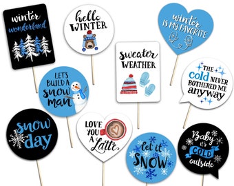 May include: A collection of winter-themed photo booth props on wooden sticks. Designs include phrases like "Winter Wonderland," "Hello Winter," and "Let's Build a Snowman," along with snowflakes and winter apparel illustrations.