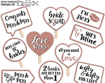 May include: Printable photo booth props with rose gold glitter and black text. The props feature phrases like "Congrats Mrs & Mrs", "Here Come The Brides", "Love Wins", "Bride Squad", "I'm Hers", "She's Mine", "All You Need Is Love", "2 Brides Are Better Than 1", and "Wifey & Wifey For Lifey".