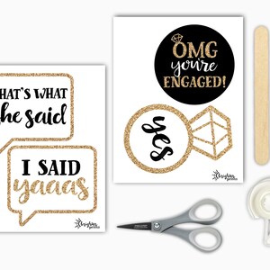 Op de afbeelding: Een set fotobooth-rekwisieten voor een verlovingsparty met gouden glitteraccenten. De rekwisieten omvatten twee spraakballonnen met de tekst "That's what she said" en "I said yaaaas", een ronde zwarte cirkel met de tekst "OMG you're engaged!" en een ring met een diamant en het woord "yes" in gouden glitter. De set bevat ook twee houten stokjes, een schaar en een rol tape.