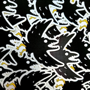 May include: A pile of black and white crow stickers with yellow accents. The crows are depicted in a flying pose with their wings spread out.
