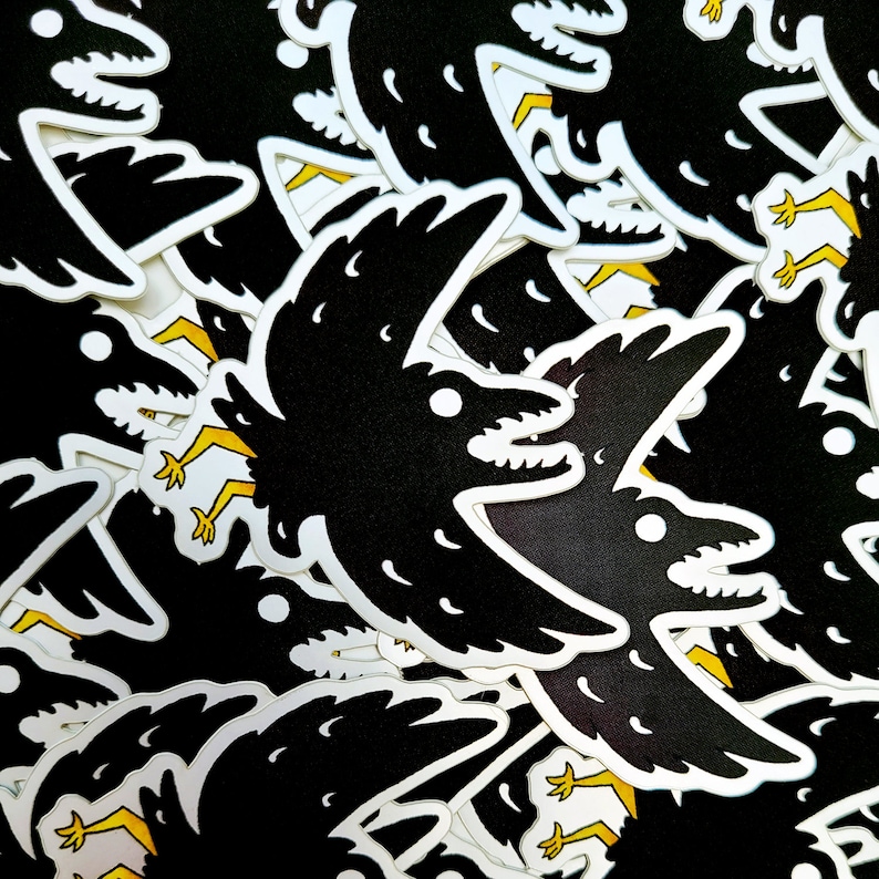 May include: A pile of black and white crow stickers with yellow accents. The crows are depicted in a flying pose with their wings spread out.