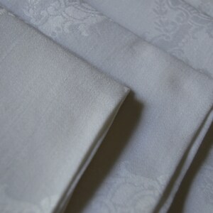 May include: A stack of four white linen napkins with a subtle embossed floral pattern.