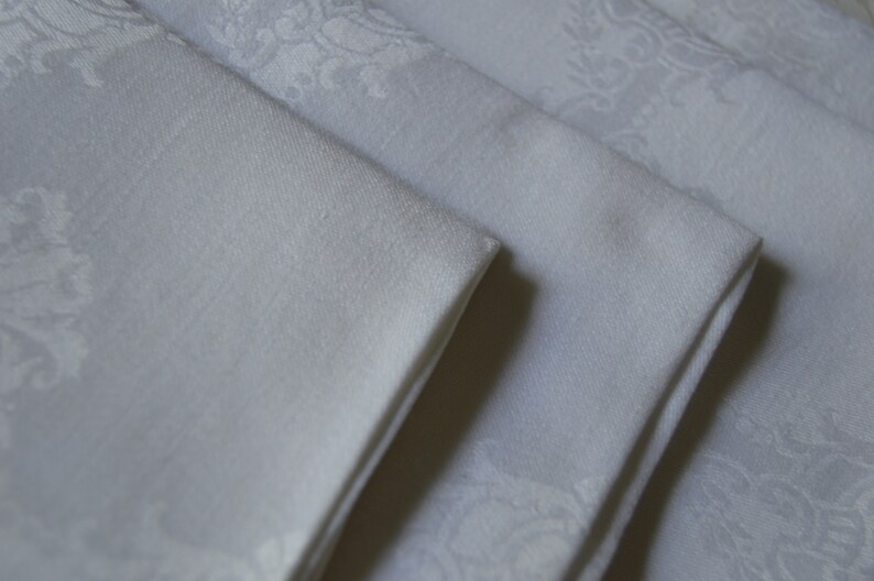 May include: A stack of four white linen napkins with a subtle embossed floral pattern.
