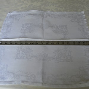 May include: White linen dinner napkin with an embroidered floral design. The napkin is folded in half and measures 18 inches by 18 inches.