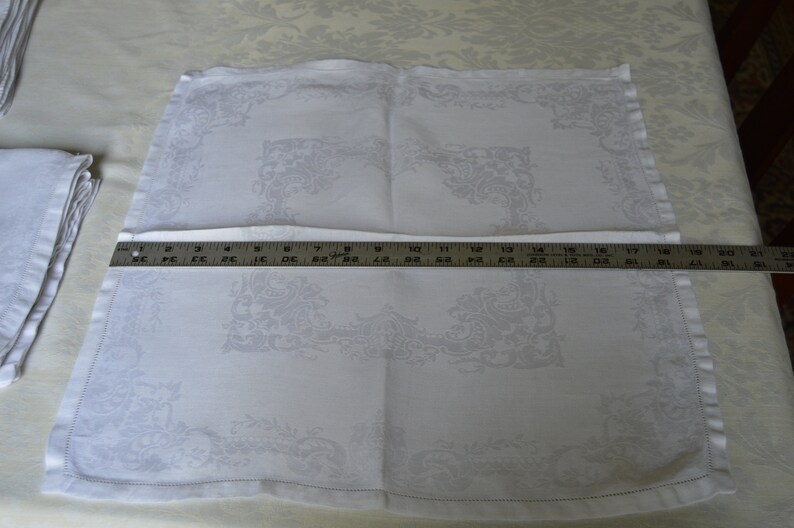 May include: White linen dinner napkin with an embroidered floral design. The napkin is folded in half and measures 18 inches by 18 inches.