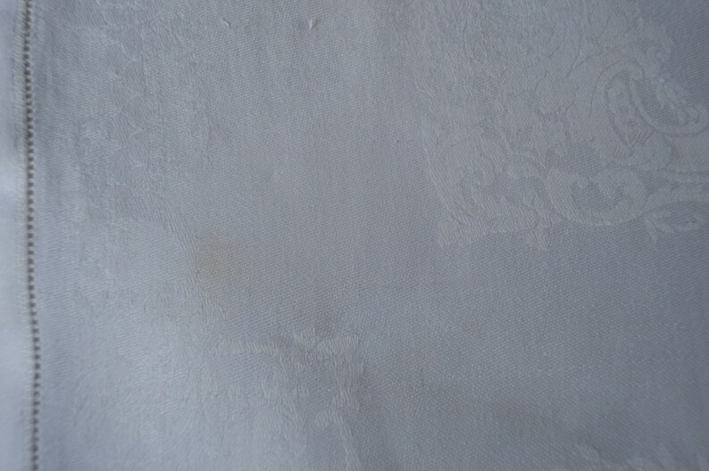 May include: A white linen tablecloth with a subtle embossed pattern. The tablecloth has a small brown stain.