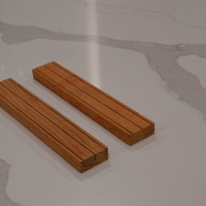 May include: Two wooden rectangular blocks, each made of multiple thin strips of wood, are placed side by side on a white surface.