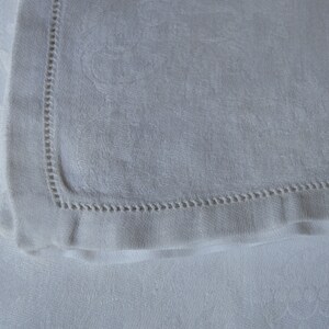 May include: A white linen napkin with a delicate embroidered border. The napkin is folded in half and has a soft, textured surface.