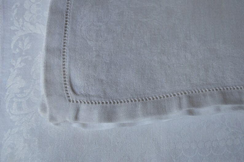 May include: A white linen napkin with a delicate embroidered border. The napkin is folded in half and has a soft, textured surface.