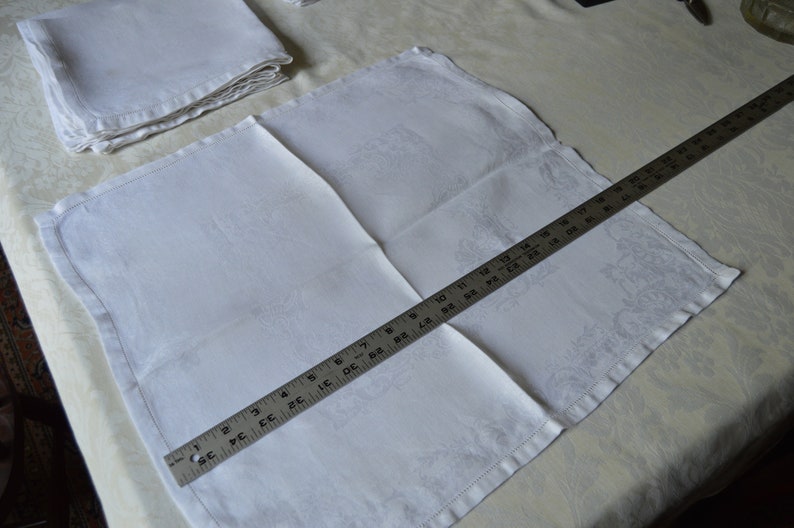 May include: A white linen napkin with a subtle embossed pattern, folded and measured with a ruler. The ruler shows 18 inches.