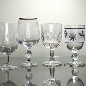 May include: Six clear glass wine glasses with different designs. The glasses are arranged in a row on a white surface.