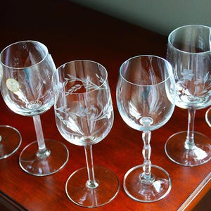 May include: Six clear glass wine glasses with etched designs. The glasses are arranged on a wooden surface.