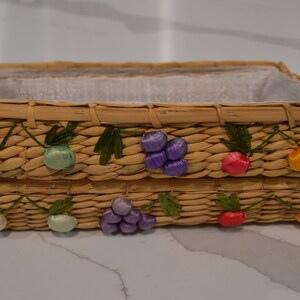 May include: Two woven wicker baskets with handles. The baskets are decorated with colorful fruit designs, including green, purple, and orange.