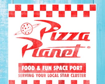 May include: A white sign with red checkered borders and the words "Pizza Planet" in red. The logo features a red pizza with a planet ring around it. The text "Food & Fun Space Port" and "Serving Your Local Star Cluster" are also in red.