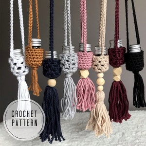 May include: A set of seven crocheted bottle holders with tassels in various colours, including white, brown, black, grey, pink, beige, and burgundy. Each holder has a small glass bottle with a silver lid. The holders are hung from a string and have a wooden bead at the bottom.