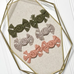 K&ouml;nnte beinhalten: Sechs handgefertigte Makramee-Ornamente in verschiedenen Farben, darunter Gr&uuml;n, Beige und Rosa. Die Ornamente werden auf einem goldenen Tablett aus Metall pr&auml;sentiert.
