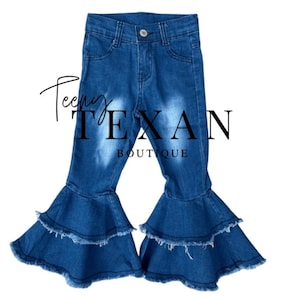 May include: Blue denim bell bottom jeans with a frayed hem and multiple layers of ruffles. The jeans have a distressed look and are designed for children.
