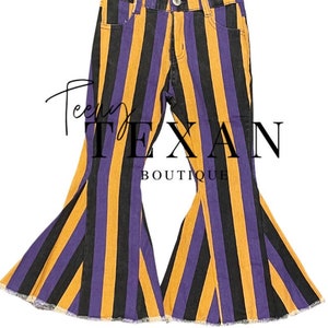 May include: Purple, black, and gold striped flared jeans with a frayed hem. The jeans are a children's size and have a 'Teen Texan Boutique' logo on the back.