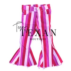 May include: Pink and red striped bell bottom jeans with a frayed hem. The jeans are made of denim and have a casual style.