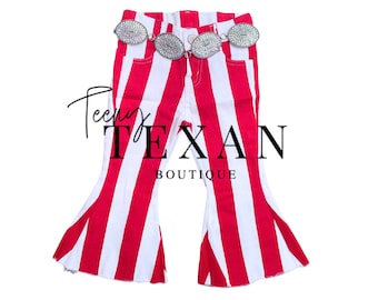 May include: Red and white striped bell-bottom pants with a rhinestone belt. The pants have a flared leg design and the text "Teeny Texan Boutique" is visible.