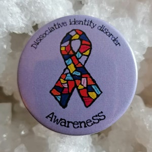 May include: Purple button with a colorful ribbon and the text "Dissociative Identity Disorder Awareness".