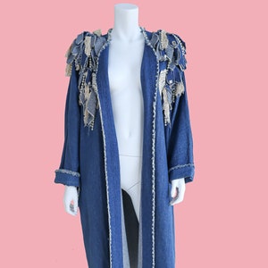 Può includere: Una lunga giacca di jeans con bordi sfrangiati e un bordo decorativo in tessuto all'uncinetto sulle spalle.