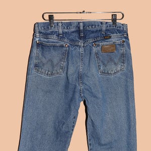 May include: A pair of blue denim jeans with a brown leather patch on the back pocket that says "Wrangler".