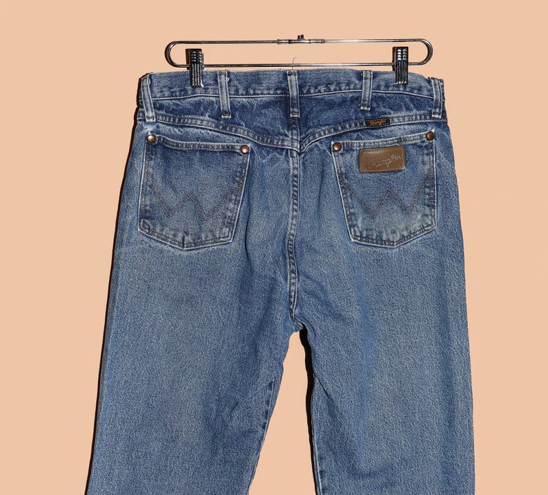 May include: A pair of blue denim jeans with a brown leather patch on the back pocket that says "Wrangler".