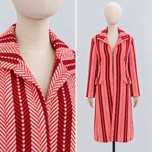 May include: A long-sleeved coat featuring a bold vertical herringbone pattern in alternating stripes of bright red, dark maroon, and white. The coat has a notched lapel collar, two front flap pockets, and a straight, knee-length silhouette.
