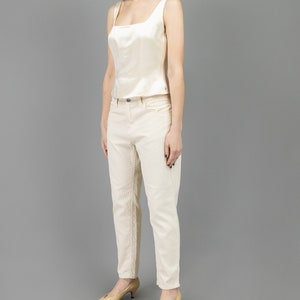 collector of vision model is wearing a size medium cream escada silk corset showing off the side with square neckline, thick straps, styled with cream corduroy pants, nude low pumps, and crystal dangling earrings