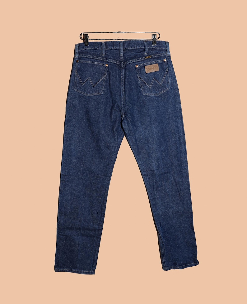 May include: A pair of dark blue denim jeans with a brown leather patch on the back pocket that says "Wrangler".