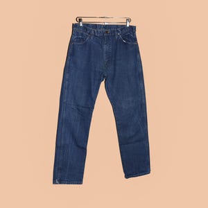 May include: A pair of dark blue denim jeans hanging on a hanger. The jeans have a classic straight leg style and a button fly.