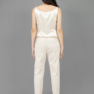 collector of vision model is wearing a size medium cream escada silk corset showing off the back with scoop neckline, thick straps, styled with cream corduroy pants, nude low pumps