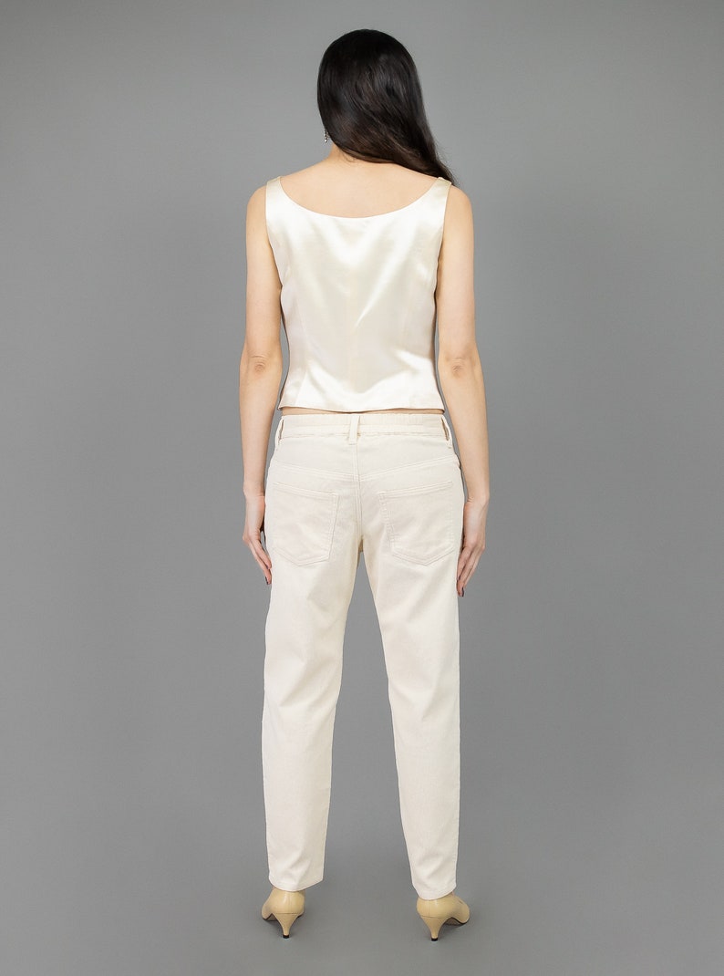 collector of vision model is wearing a size medium cream escada silk corset showing off the back with scoop neckline, thick straps, styled with cream corduroy pants, nude low pumps